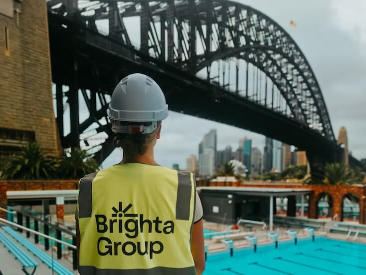Lady standing facing a bridge in Sydney with Brighta Group wearing a high vis vest